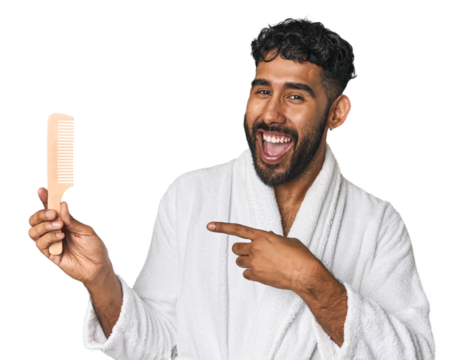 Hispanic male with comb in studio smiling and pointing aside, showing something at blank space.