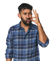 Young Hispanic man isolated with fingers on lips keeping a secret.