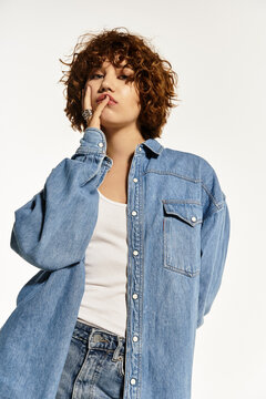 Curly-haired woman in denim shirt and jeans shows summer vibes against white backdrop
