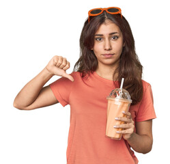 Middle Eastern woman with smoothie showing a dislike gesture, thumbs down. Disagreement concept.