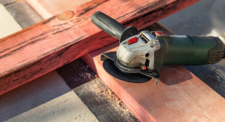 Electric angle grinder, commonly known as a grinder , resting on top of two wooden beams.