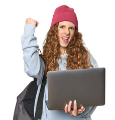 Redhead young woman student with laptop raising fist after a victory, winner concept.