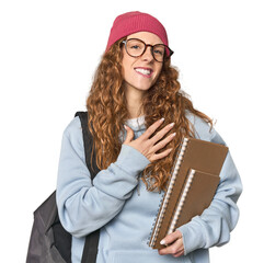 Redhead caucasian young woman student with books laughs out loudly keeping hand on chest.