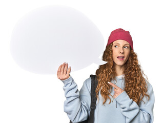 Redhead holding a comic speech bubble smiling and pointing aside, showing something at blank space.