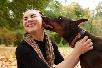 Close-up of beautiful smiling Caucasian girl and Doberman pinscher outside in autumn park. Caring...
