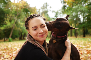 Close-up of beautiful smiling Caucasian girl and Doberman pinscher outside in autumn park. Caring...