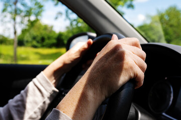 Female hands on the vehicle steering wheel, inside the car, driving through countryside