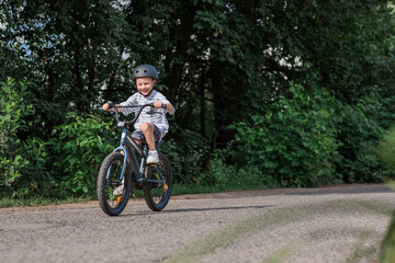 Fototapeta premium A beautiful 6-year-old boy riding a bicycle in a protective helmet outside. A happy child engaged in an active sport. Protection. Life insurance and child safety.