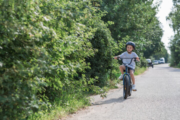 Obraz premium A beautiful 6-year-old boy riding a bicycle in a protective helmet outside. A happy child engaged in an active sport. Protection. Life insurance and child safety.