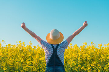 Successful female farmer with hands raised in cultivated rapeseed field