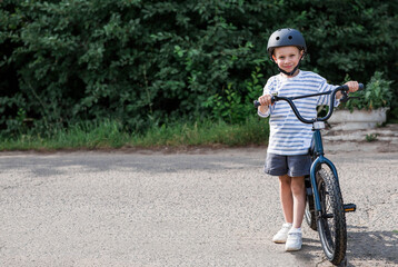 Fototapeta premium A beautiful 6-year-old boy riding a bicycle in a protective helmet outside. A happy child engaged in an active sport. Protection. Life insurance and child safety.