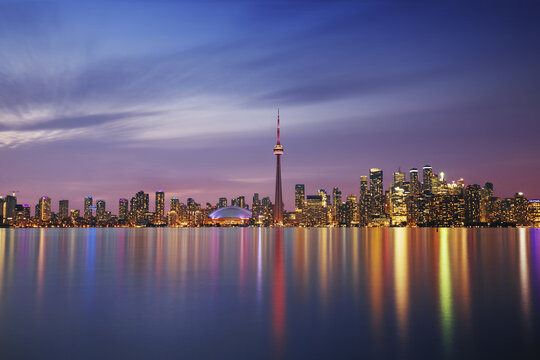Aerial view of the illuminated cityscape reflecting on the tranquil waters, dominated by the CN Tower and Rogers Centre against a twilight sky, Toronto, Ontario, Canada.