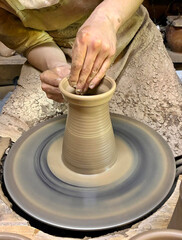 Vase made of raw clay in process of being hand-made by master, hands of young potter pulling out...