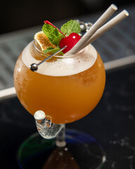 ibrant orange alcoholic cocktail, served in a unique round glass with a stem, is garnished with...
