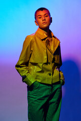 Young woman posing confidently in a shiny yellow jacket and green pants against a vibrant gradient...