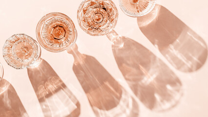Wine Glasses of rose wine on pink background, sun flare and reflection from sunlight. Aesthetic...