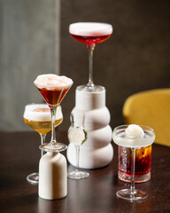 collection of five distinct alcoholic cocktails, varying in color and presentation, are artfully arranged on a dark table against a blurred background