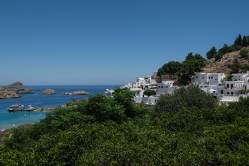 Lindos village on the Greek island of Rhodes. Perched on the hillside, this tranquil Mediterranean village boasts whitewashed buildings overlooking crystal-clear blue waters.
