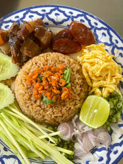 Close up shot of Thai shrimp paste fried rice with shallot, sweet barbeque pork, fried egg, vegetable and spicy chili.