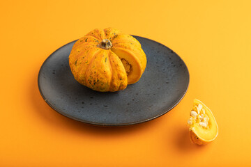 Orange Pumpkin cutted on blue plate on orange pastel paper. Side view, copy space