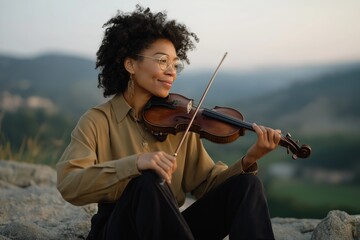 Fototapeta premium African female young adult playing violin outdoors in serene landscape