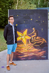 Young asian male with glasses, short black hair, stands beside large painting of man rowing under...