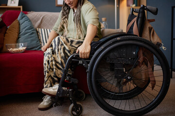 Young woman with disability sitting in wheelchair indoors, holding wheel with one hand, wearing...