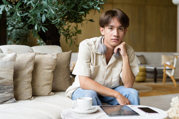 Non binary Asian student man sitting in modern coffee shop wearing headphones