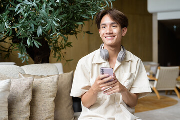 Non binary Asian student man sitting in modern coffee shop using phone