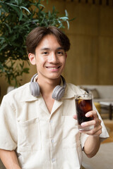 Non binary Asian student man sitting in modern coffee shop drinking cola