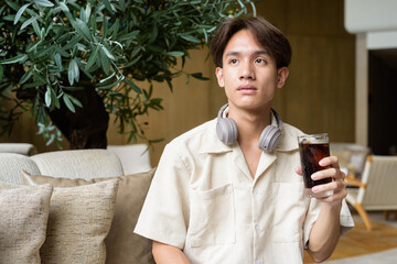 Non binary Asian student man sitting in modern coffee shop drinking cola