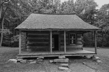 Black and white photograph of the Carter Shields cabin in Cades Cove, showing the front door, covered porch, and the rocks used to support and level the cabin.
