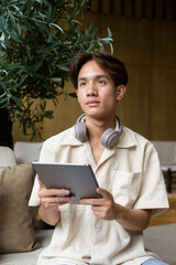 Non binary Asian student man sitting in modern coffee shop using digital tablet computer