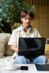 Non binary Asian student man sitting in modern coffee shop using laptop computer