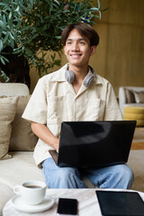 Non binary Asian student man sitting in modern coffee shop using laptop computer