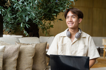 Non binary Asian student man sitting in modern coffee shop using laptop computer