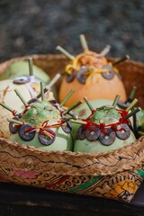Close-up of decorated coconuts in a woven basket. The coconuts are adorned with coins and bamboo sticks, for a cultural celebration in Ubud, Bali, Indonesia