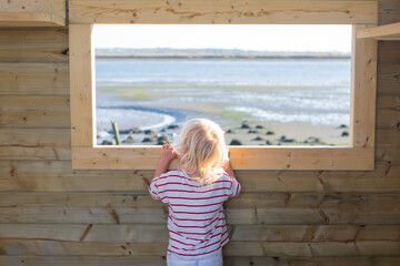 Blonde girl watching birds through a window in a birdwatching hut
