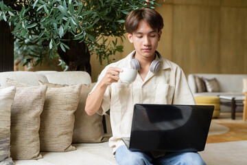 Non binary Asian student man sitting in modern coffee shop using laptop computer