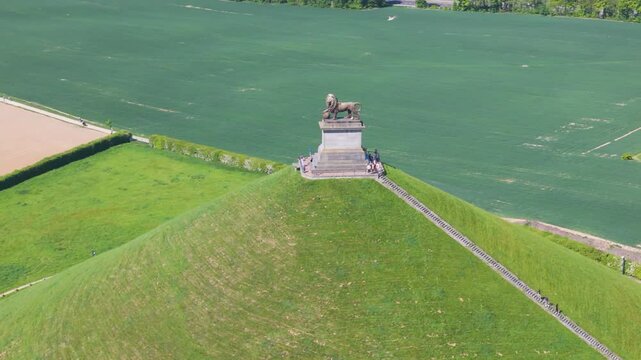 complete monument visitors descend stairs surrounded by green grass trees open fields lion's mound waterloo belgium scene reflects dynamic drone panning shot leeuw van 
