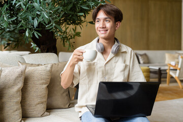 Non binary Asian student man sitting in modern coffee shop using laptop computer