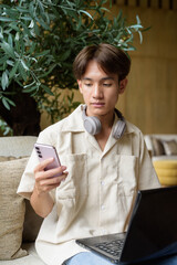 Non binary Asian student man sitting in modern coffee shop using laptop computer