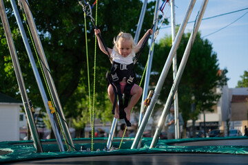 Little European Girl Learning to Jump on a Trampoline with Safety Harness. Summer Fun
