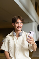 Non binary Asian student man sitting in modern coffee shop using phone