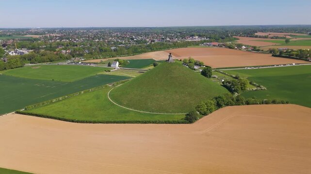 complete monument alongside parking town buildings surrounded by green grass trees open fields lion's mound waterloo belgium perspective reveals circling drone shot leeuw van 
