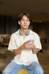 Non binary Asian student man sitting in modern coffee shop using phone