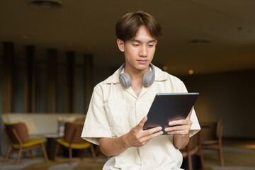 Non binary Asian student man sitting in modern coffee shop using digital tablet computer