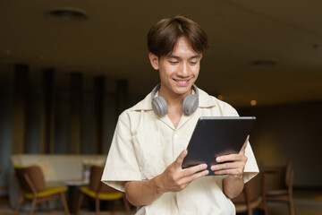 Non binary Asian student man sitting in modern coffee shop using digital tablet computer