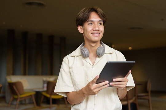 Non binary Asian student man sitting in modern coffee shop using digital tablet computer