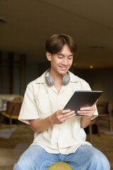 Non binary Asian student man sitting in modern coffee shop using digital tablet computer